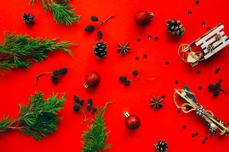 Winter composition with fir tree branches, decorative balls, cones and sequins on bright red background. Top view. Flat layの写真素材