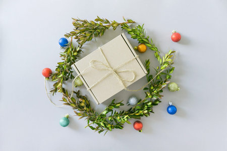 Craft present box on pastel background with boxwood brunches and decorative balls. Christmas gift....