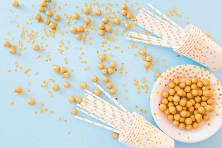 Birthday or party paper glasses with straws, dish and golden sequins on blue background. Festive concept. Flat lay style. Top view.の写真素材
