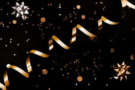 Golden streamer, decorative bows and sequins on black background. Party and festive concept. Top view. Flat lay.の写真素材