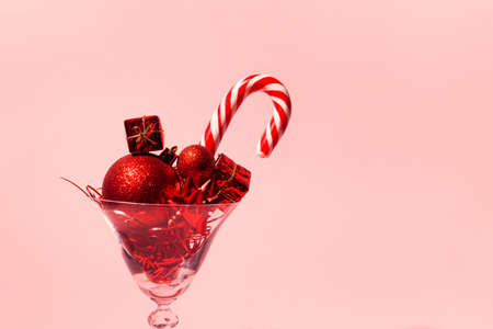 Martini glass close up with red decorative baubles, present boxes and lollipop on pink pastel background. Party and festive concept.の写真素材