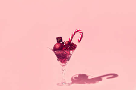 Creative composition made of martini glass with red decorative baubles, present boxes and lollipop on pink pastel background. Party and festive concept.の写真素材