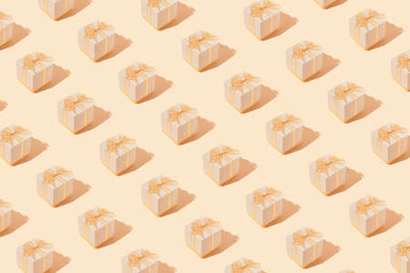 Creative pattern made with present boxes with bows on pastel beige background. Christmas or birthday party concept. Minimal style.の写真素材