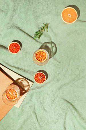 Summer scene with fruits, rosemary, glass of water and books on pastel green beach towel. Drinks and...