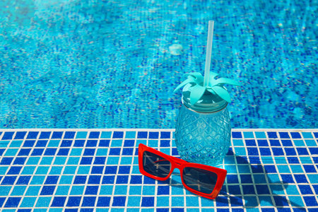 Fresh cocktail with straw and red sunglasses by the swimming pool. Vacation and travel concept....