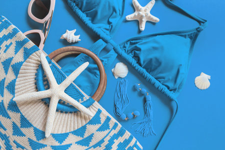 Woman's beach accessories: bikini, bag, sunglasses, earrings, starfish and shells on bright blue...