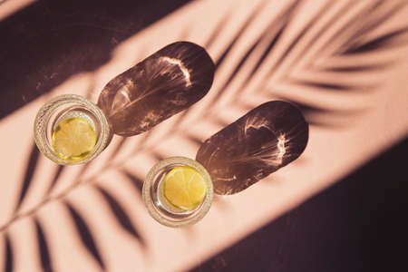 Two glasses of water with sliced lemon on sunlit background with shade. Summer refreshment concept. Minimal style.Top view. Flat layの写真素材