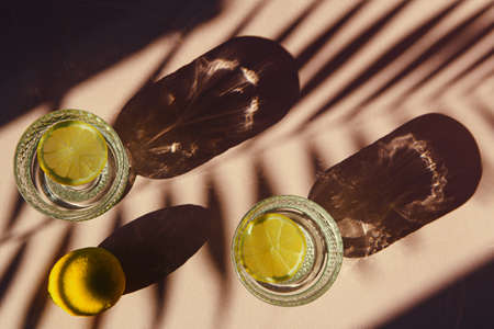 Two glasses of water with sliced lemon on sunlit background with shade. Summer refreshment concept. Minimal style. Top view.の写真素材