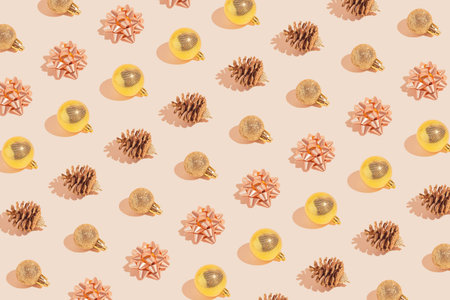 Creative pattern made golden bows, cones and baubles on pastel beige background. Christmas or...