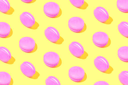Creative pattern made of pink macaroons on yellow background. Dessert and confectionary concept.の写真素材