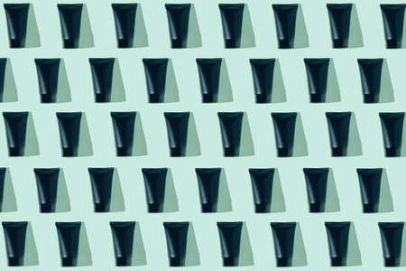 Creative pattern made of black cosmetic tube on pastel green background with sunlit. Skincare concept. Minimal styleの写真素材
