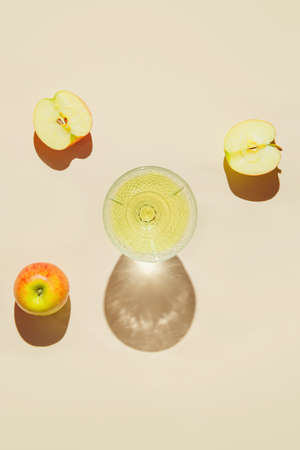 Creative composition made of glass with fruit juice and apples on pastel beige sunlit background with shadows. Summer and refreshment concept. Harvest themeの写真素材