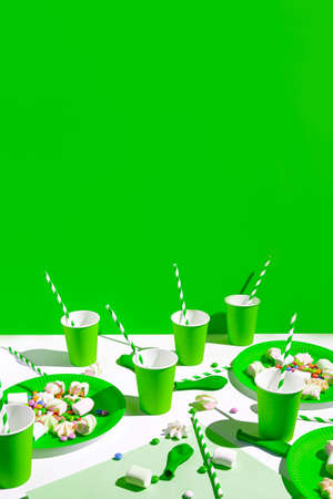 Creative composition made of green paper glasses with straws, dishes, meringues and balloons. Festive concept. Birthday and party background.の写真素材