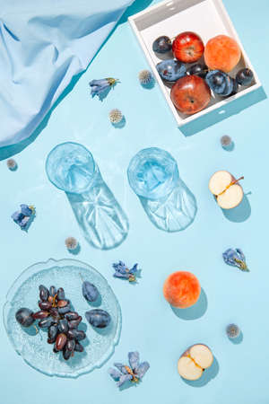 Creative composition made of plate with fruits, glasses, apples and peach on pastel blue sunlit background with cloth and shadows. Summer and refreshment concept. Harvest theme. Top view. Flat layの写真素材