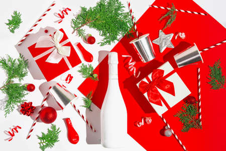 Christmas composition made of white champagne bottle, present boxes, silver paper glasses with straws, green needles branches, red baubles and balloons. Festive and party concept background. Top view. Flat layの写真素材