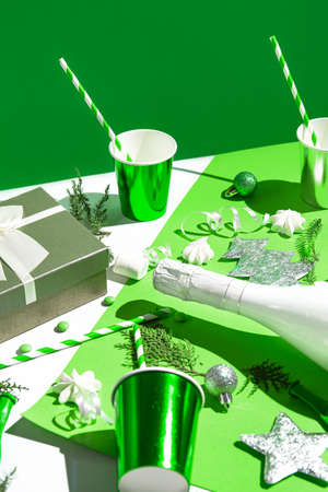 Christmas composition made of paper glasses with straws, present box, white champagne bottle, meringues and green baubles. Festive and party concept. 2022 new year background.の写真素材