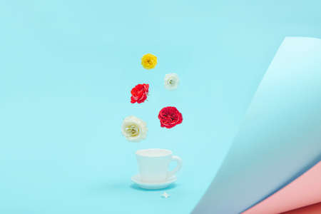 Creative composition made of white cup of coffee or tea with flying rose flower buds on pastel blue background. Morning beverage concept.の写真素材