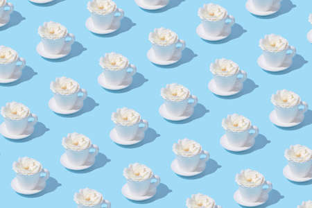 Creative pattern made of white cup of coffee or tea with rose flower bud on pastel blue background. Morning beverage concept. Minimal styleの写真素材