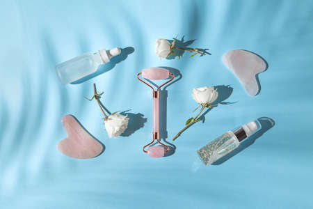 Cosmetic facial kit for home skin care and spa. Face roller and gua sha massagers, bottle of essential oil and serum on blue pastel sunlit background with shadows. Natural treatment concept. Top view. Flat layの写真素材
