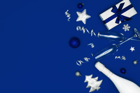 Christmas composition made of white champagne bottle, present box, two glasses on bright blue background. Festive and party concept background. Top view. Flat layの写真素材