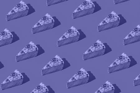 Creative pattern made of piece of cheesecake on violet background. Healthy dessert concept. Minimal style. Color of the 2022 inspiredの写真素材