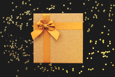 Golden present box with bow on black background with sequins. Christmas or birthday gift....