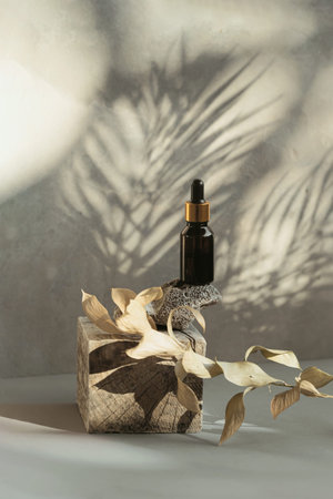 Amber glass bottle of essential oil or serum with pipette on wooden podium with gray concrete wall...