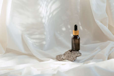 Amber glass bottle of essential oil or serum with pipette on white fabric background with shadows. natural skin care cosmetic conceptの写真素材