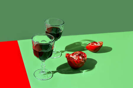 Creative composition made of glass of red wine or juice and pomegranates on green backgound with sunlit and shadows. Summer refreshment concept. minimal style.の写真素材