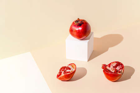 Creative composition madeof red pomegranates on pastel sunlit backgound with white cube podium. Summer refreshment concept. minimal style.の写真素材