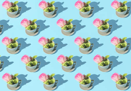 Creative pattern made of cup of coffee or tea with pink rose flower bud on pastel blue background. Morning beverage concept. Minimal styleの写真素材