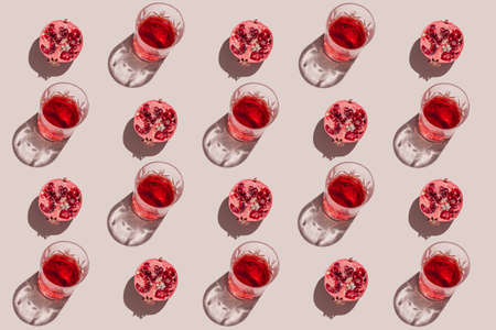 Creative pattern made of a half of pomegranate and glass with juice or red wine on pastel beige background. Summer fruit and refreshment concept. minimal style. Sunlit flat lay. top viewの写真素材