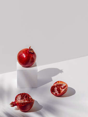 Creative composition madeof red pomegranates on sunlit backgound with white cube podium and shadows. Summer refreshment concept. minimal style.の写真素材