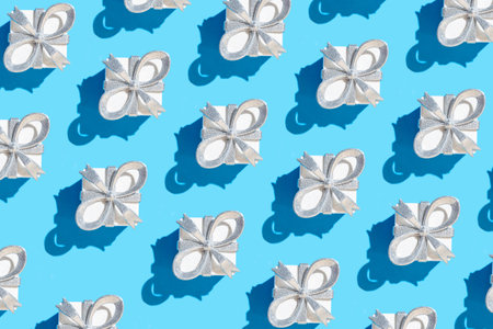 Creative pattern made with glittering white present boxes with silver bow on pastel blue background. Christmas or birthday gift concept. holiday theme. minimal style.の写真素材
