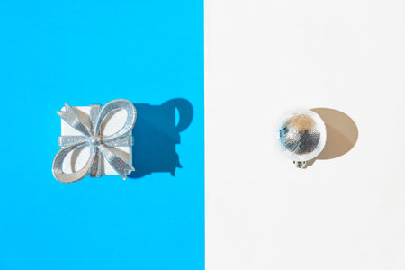 Creative composition made of silver present box and decorative ball on white and blue background...