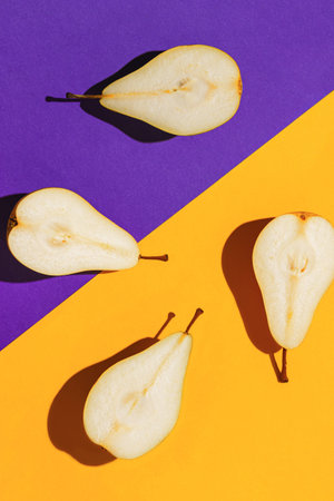 Creative layout made of raw sliced pears on bright violet and orange geometric background with...
