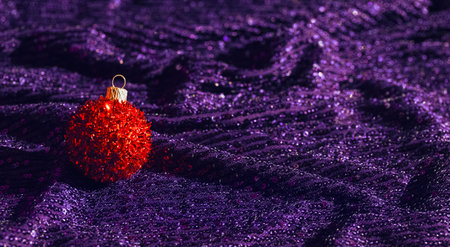 Red christmas bauble on shimmering violet background with sequins. Minimal style xmas composition. Celebration and party conceptの写真素材