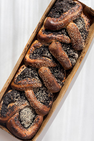 Sweet homemade bread braided with poppy seeds on craft paper and white sunlit backgroundの写真素材