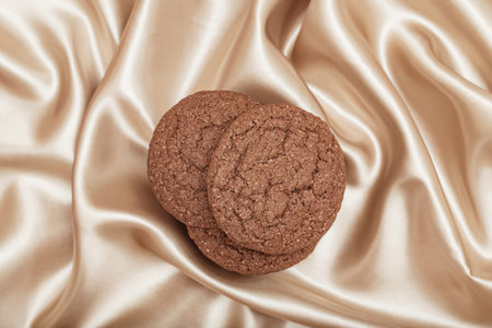 Brown american cookies on beige silk fabric background. Minimal style. Bakery and pastry concept. Top viewの写真素材