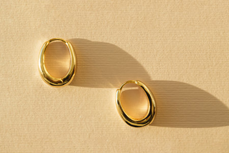 Gold earrings closeup on pastel background with shadow. Concept of stylish women's accessoriesの写真素材