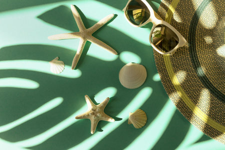 Creative summer composition with trendy sunglasses, hat, starfishes and shells on background with monstera leaf shadow. Vacation conceptの写真素材