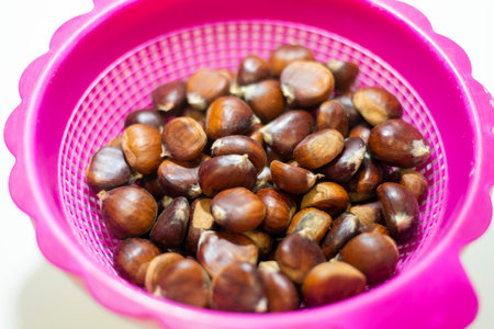 Chestnuts in a pink plastic colander on a white background.の写真素材