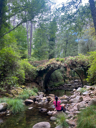 Woman sitting on a stone bridge over a stream in the forest.の写真素材