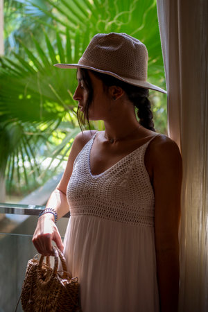 Beautiful woman wearing hat and white dress, looking out the window. Spanish brunette woman European womanの写真素材