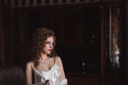 a curly-haired young girl standing in a room wearing a light-weight sexy robeの写真素材