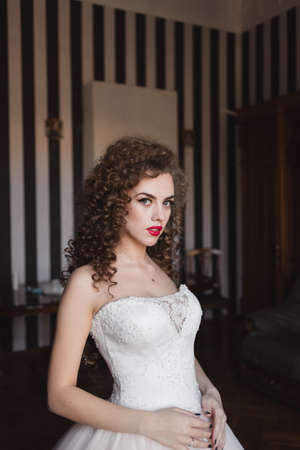 portrait of a curly-haired bride girl standing at a window and looking forwardの写真素材