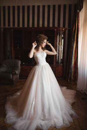 a bride with a beautiful figure dressed in a lavish wedding dress is standing in a komtna at the window raising her hands up and dancingの写真素材