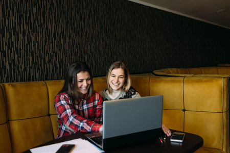 two young girls sitting at the table with a laptop in a cafe and smiling cheerfully