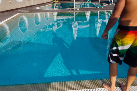 a young guy with a sporty physique stands near the pool on it dressed in swimming trunksの写真素材