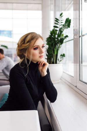 Beautiful young girl sitting in a cafe, and looks thoughtfully out theの写真素材